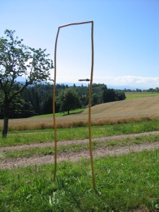  In der Landschaft steht, von drei goldenen Haselzweigen umrissen, eine imaginre Tre.  Ein alter Schlssel und eine alte  Klinke sind rechts angebracht. Die Trklinke schafft die Mglichkeit des hindurch-Gehens. Wre lediglich der Rahmen da, der den Raum begrenzt, wrde das zum Betrachten des "Bildes" einladen. So ist es aber eine Tre, die auffordert hindurchzugehen. Der Schlssel, der "steckt", weist auf die momentane Mglichkeit und Berechtigung dazu hin; aber auch auf die Verschliebarkeit, und somit darauf, da hinter der Tre etwas Geheimnisvolles, Wertvolles stecken knnte.